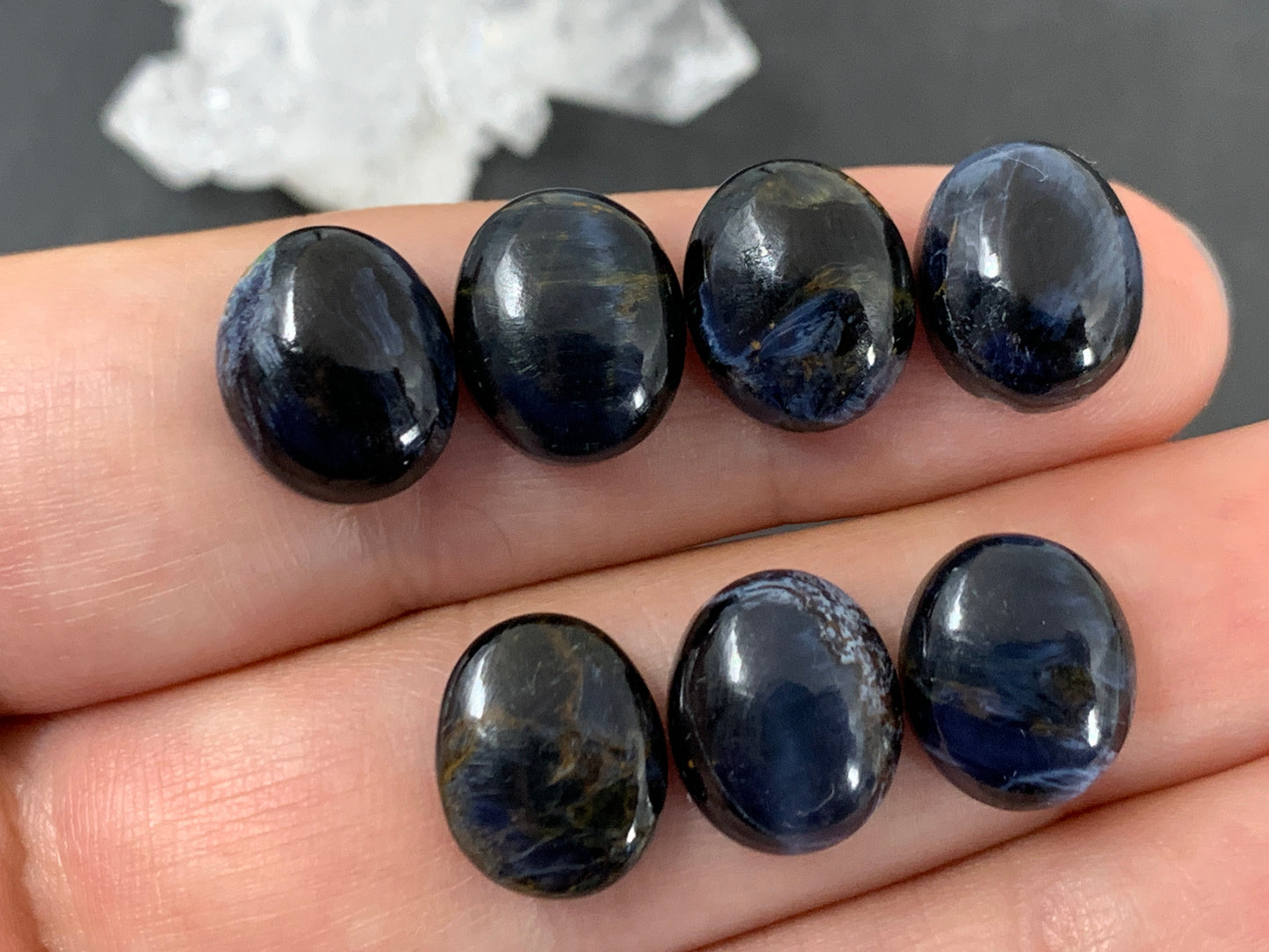 A hand holding several dark blue gemstones, possibly sapphires or amethysts, against a dark background.