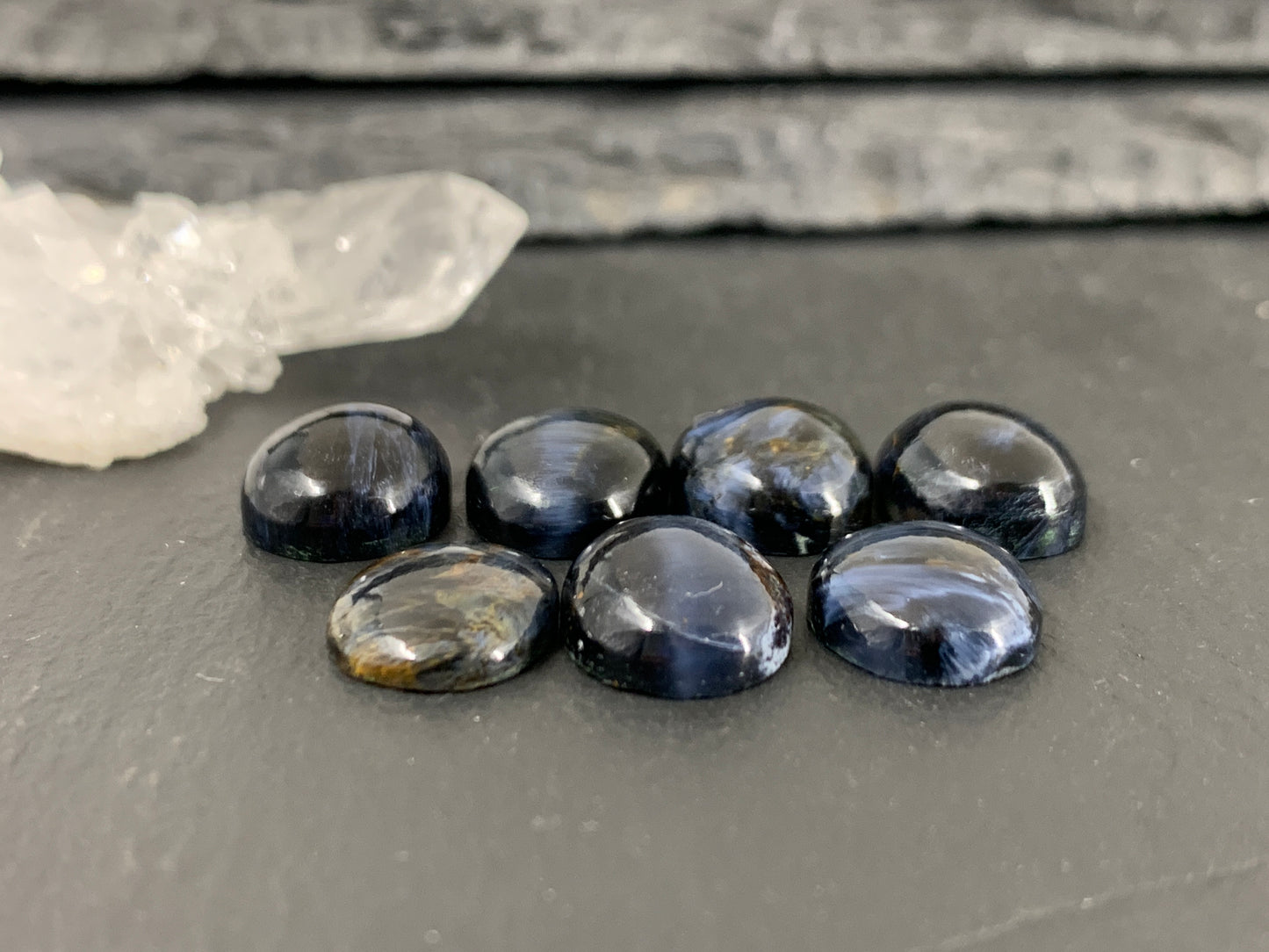 a collection of seven dark blue gemstones, possibly sapphires or amethysts, arranged on a gray surface.