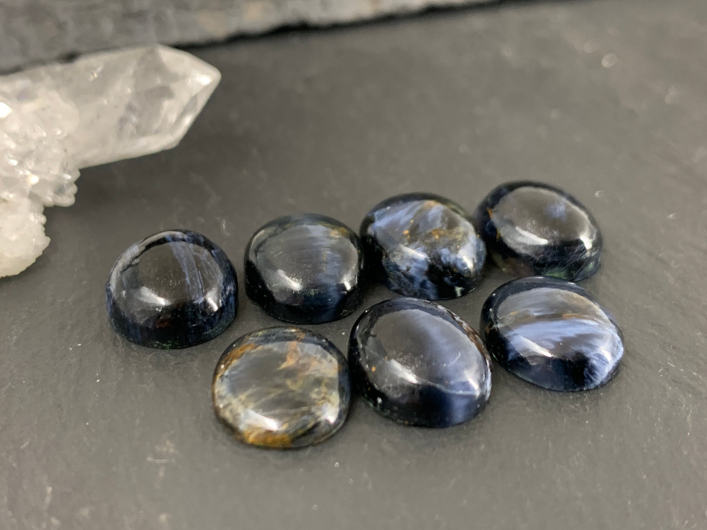 a collection of seven dark blue gemstones, including a clear crystal, arranged on a gray surface.