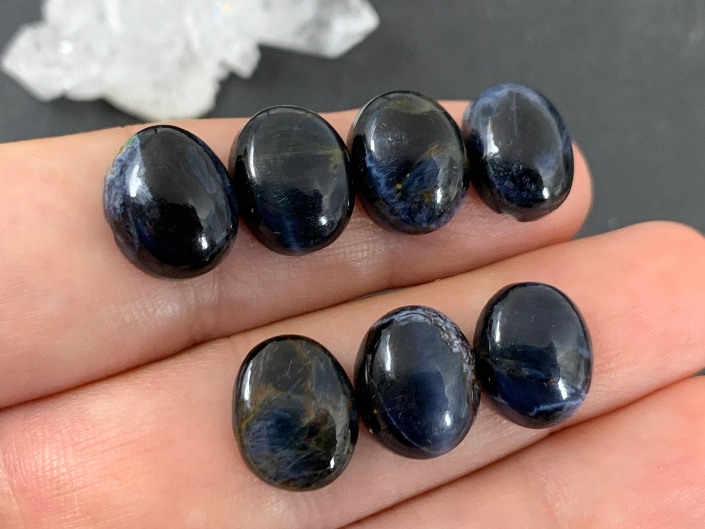 A hand holding several dark blue gemstones, possibly sapphires or amethysts, against a dark background.