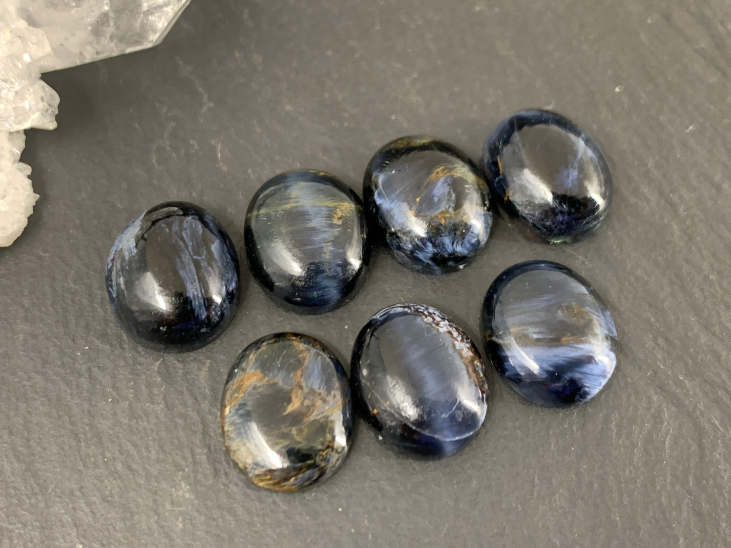 a collection of seven dark blue gemstones arranged on a gray surface.