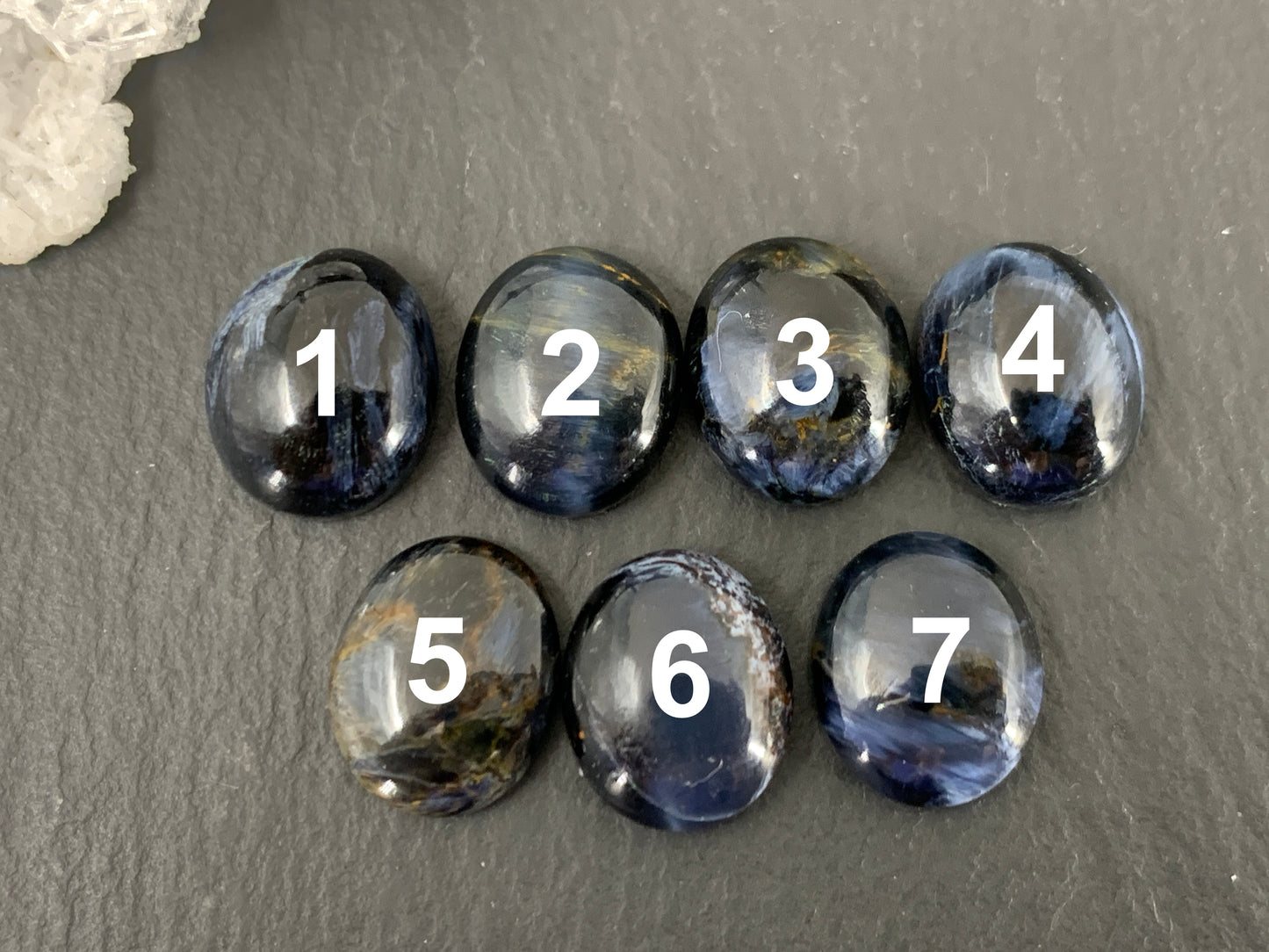 a collection of seven round, black gemstones with numbers 1 through 7 on them, arranged in a row on a gray surface.