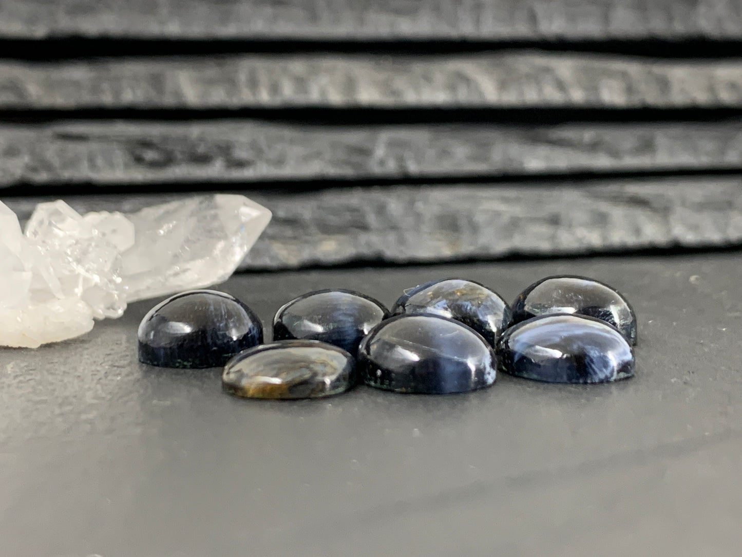 A collection of seven dark blue gemstones, including a crystal and a piece of quartz, arranged on a gray surface.