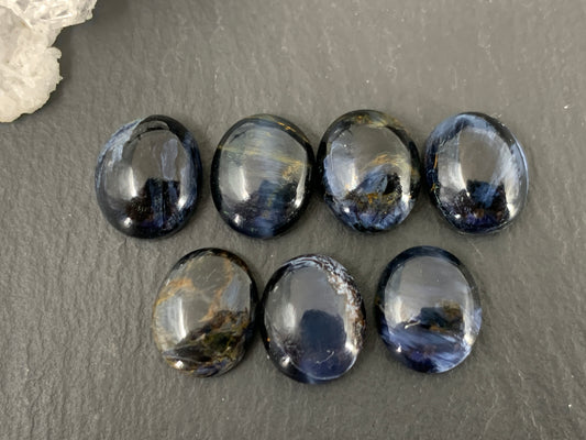 a collection of nine dark blue gemstones arranged in a row on a gray surface.